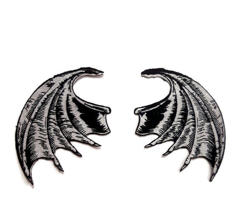 K&ouml;nnte beinhalten: Ein Paar schwarze gestickte Fl&uuml;gel mit silbernem Umriss. Die Fl&uuml;gel sind mit komplizierten Linien und Kurven verziert, was ihnen ein dramatisches und gotisches Aussehen verleiht.