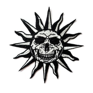 Pode incluir: Patch bordado a preto e branco com uma caveira dentro de um desenho de sol. A caveira tem uma expressão detalhada e sorridente. Os raios do sol são pontiagudos e estilizados. Adequado para casacos, malas ou outros artigos de tecido.