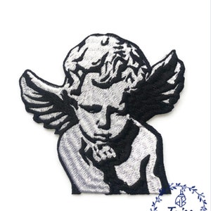 May include: Black and white embroidered iron-on patch of a cherub angel with wings. The angel is looking down with a serious expression.