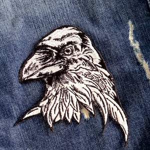 May include: Black and white embroidered raven patch on a blue denim jacket.