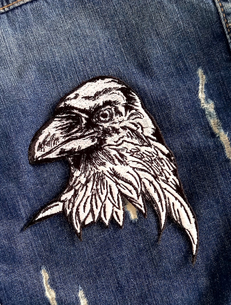 May include: Black and white embroidered raven patch on a blue denim jacket.