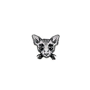 May include: A black and white patch featuring a stylized illustration of a Sphynx cat's face. The cat has large ears, multiple eyes, and whiskers. The patch is likely for clothing or accessories.