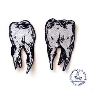 May include: Two black and white embroidered iron-on patches of teeth. The teeth are outlined in black and filled in with white. The patches are approximately 2 inches tall.