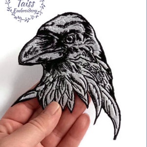May include: Black and white embroidered iron-on patch of a raven's head with detailed feathers.