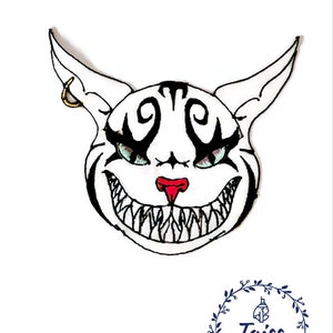 May include: White embroidered patch of a cat with a wide, toothy grin. The cat has black eyes, a red nose, and black markings on its face. The cat's ears are pointed and have a gold hoop earring on one ear.
