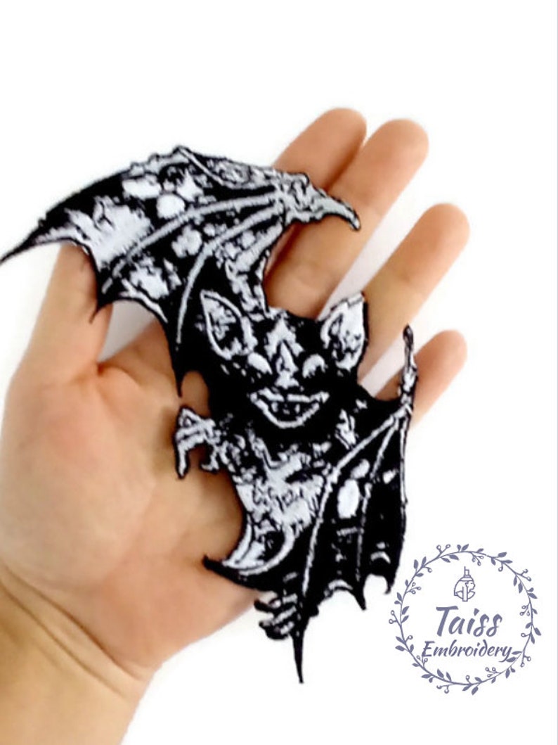 May include: Black and white embroidered iron-on patch of a bat with its wings spread. The bat has a detailed design with a menacing expression. The patch is perfect for adding a spooky touch to clothing, bags, or other accessories.