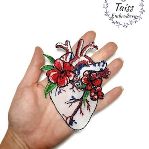May include: Embroidered patch of a red anatomical heart with red flowers and green leaves. The patch is on a white background.