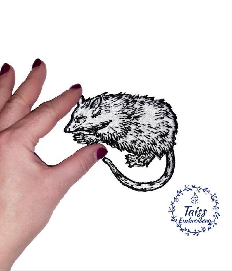May include: Black and white embroidered iron-on patch of a curled up possum. The patch is on a white background and is being held by a hand.
