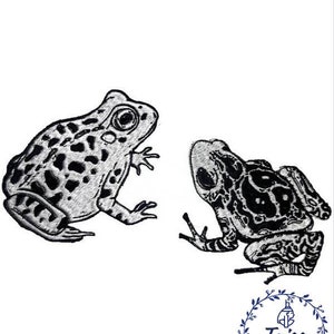 May include: Two black and white embroidered frog patches. The frogs are facing different directions. The larger frog is on the left and the smaller frog is on the right. The patches are on a white background.