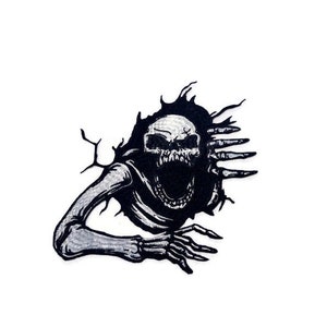 Könnte beinhalten: Schwarz-weiß gestickter Aufnäher eines Skeletts, das mit offenem Mund und ausgestreckten Krallen aus einer Wand bricht.