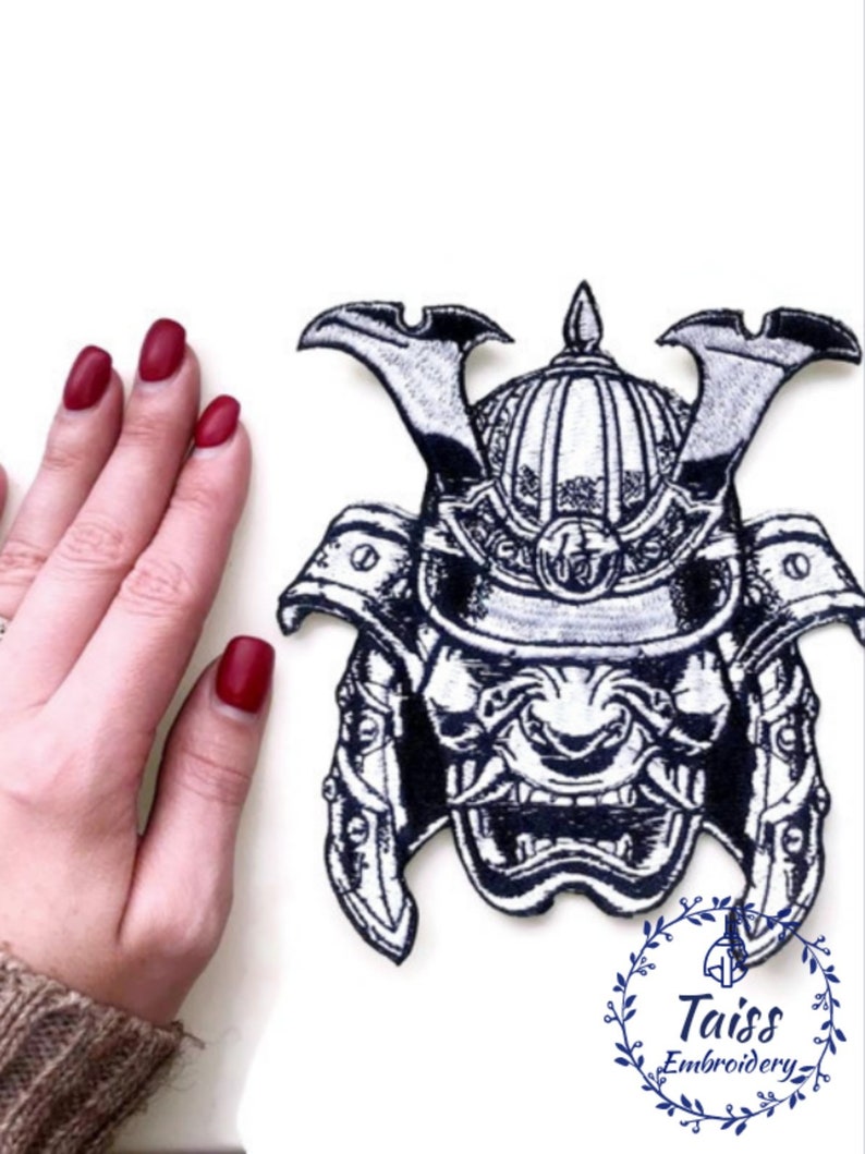 Peut inclure: Un &eacute;cusson brod&eacute; en noir et blanc repr&eacute;sentant un casque de samoura&iuml; avec une expression f&eacute;roce. L'&eacute;cusson est sur un fond blanc et est entour&eacute; d'une main.