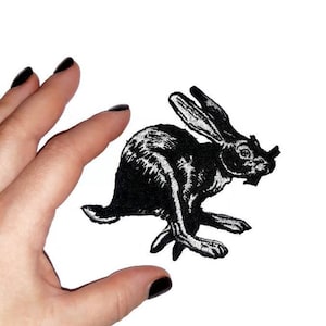 May include: Black embroidered iron-on patch of a rabbit running. The rabbit is in a vintage style.