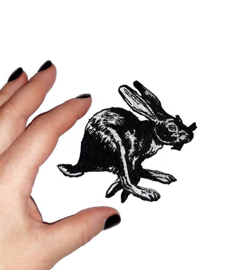 May include: Black embroidered iron-on patch of a rabbit running. The rabbit is in a vintage style.
