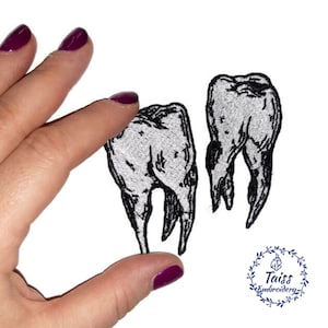 May include: Two black and white embroidered iron-on patches of teeth. The patches are on a white background.