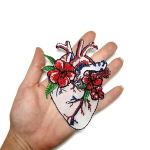 May include: Embroidered iron-on patch of a red anatomical heart with red and green flowers.