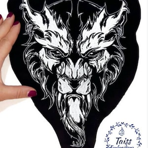 May include: Black and white embroidered patch of a wolf's face with a fierce expression. The patch is on a black fabric background. The patch is shaped like a triangle with rounded edges. The wolf's face is detailed with sharp teeth and a long tongue. The patch has the text "Taiss Embroidery" in a circle at the bottom.