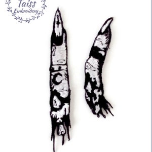 Pode incluir: Dois patches bordados em preto e branco de um dedo cortado. O dedo é costurado com um design detalhado de osso e pele.