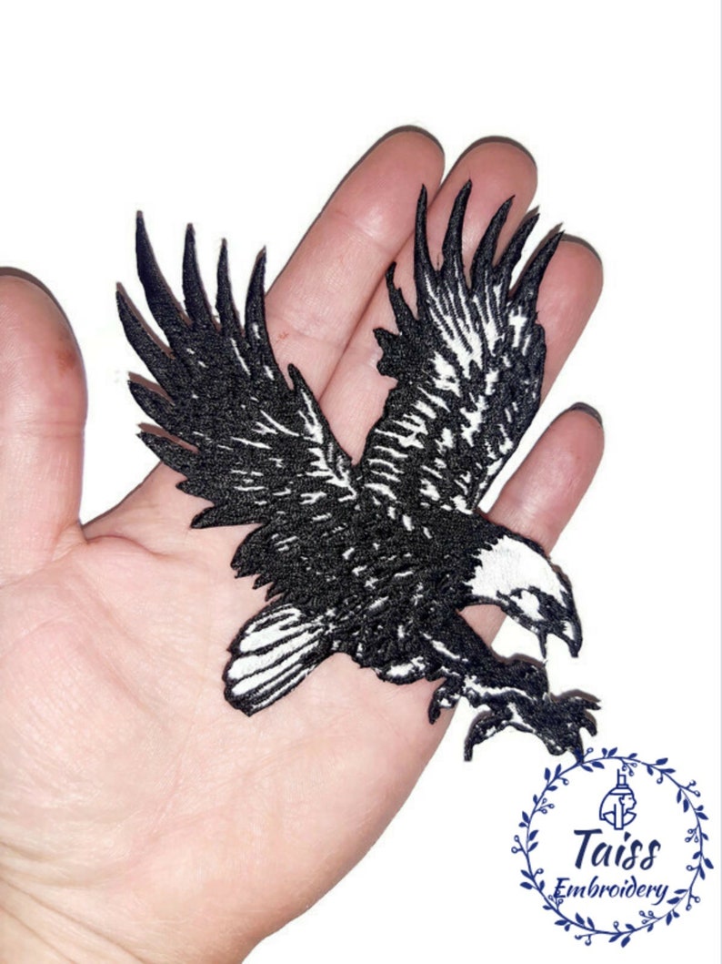 Puede incluir: Parche bordado en blanco y negro de un &aacute;guila en vuelo. El &aacute;guila est&aacute; mirando hacia la derecha y tiene las alas extendidas. El parche est&aacute; en una mano para referencia de tama&ntilde;o.