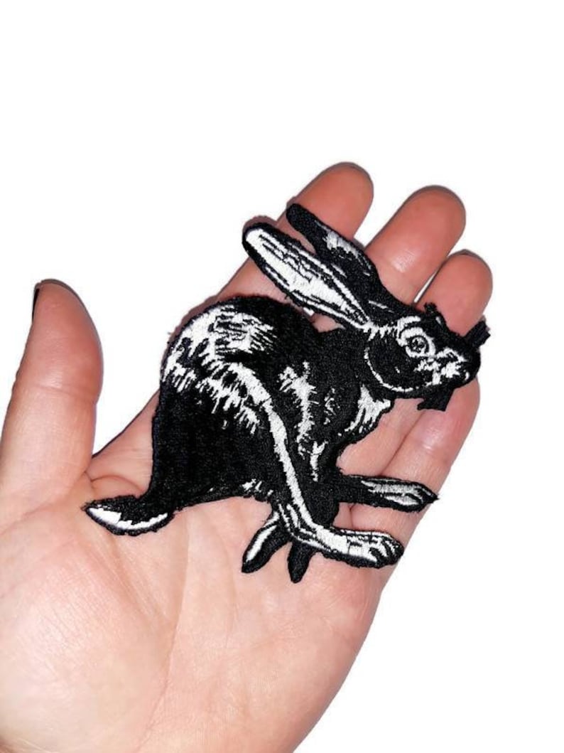 May include: Black and white embroidered iron-on patch of a rabbit running. The rabbit is outlined in white and filled in with black.