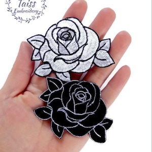 Peut inclure: Deux patchs brodés à repasser en forme de roses. Une rose est blanche avec des contours noirs, et l'autre est noire avec des contours blancs.