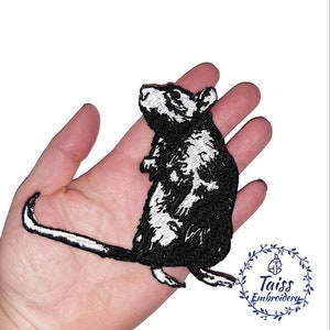 Pode incluir: Etiqueta bordada em preto e branco de um rato para passar a ferro. O rato está em pé sobre as patas traseiras com o rabo enrolado atrás.