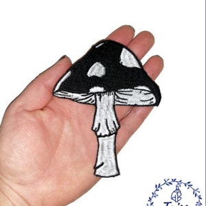 May include: Black and white embroidered iron-on patch of a mushroom with white spots on the cap.