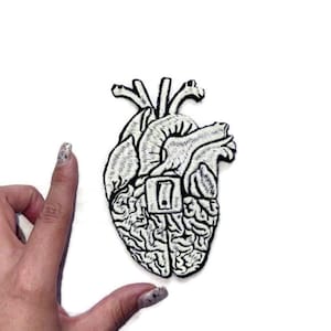 Può includere: Toppa ricamata bianca di un cuore umano con un cervello all'interno. Il cuore è contornato da filo nero.