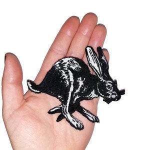 May include: Black and white embroidered iron-on patch of a running rabbit. The rabbit is facing right and has long ears.