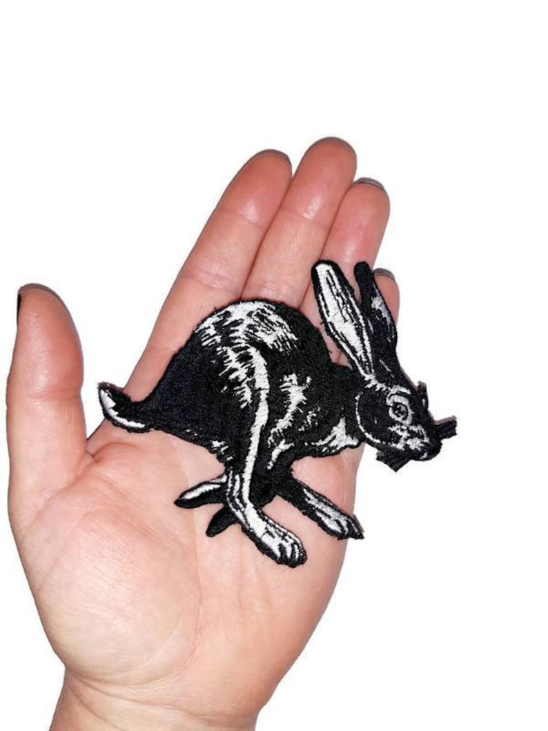 May include: Black and white embroidered iron-on patch of a running rabbit. The rabbit is facing right and has long ears.
