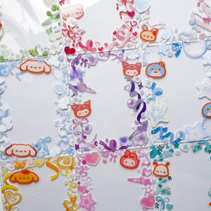 May include: A collection of clear, decorative stickers featuring cartoon characters, hearts, ribbons, and stars. The stickers are in various colors, including pink, purple, blue, and yellow. The stickers are arranged in a grid pattern.
