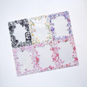 May include: Six rectangular clear plastic photo frames arranged in a grid. Each frame features a distinct decorative border: one with black and white roses, one with yellow and white flowers, one with purple floral patterns, and three with pink cherry blossoms.