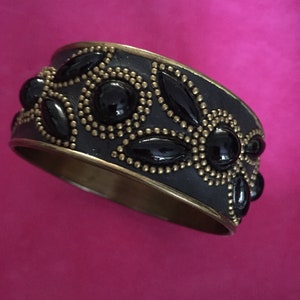 May include: A black and gold bangle bracelet with a decorative design of black stones and gold beads.