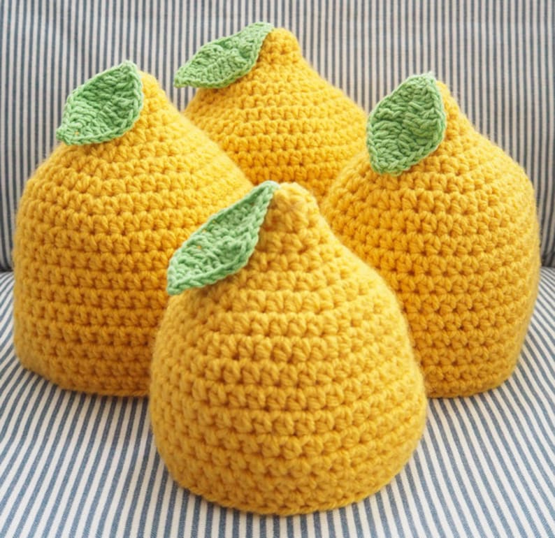 Puede incluir: Tres almohadas de punto de crochet con forma de lim&oacute;n y hojas verdes. Las almohadas son amarillas y tienen una superficie texturizada.