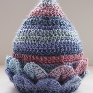 K&ouml;nnte beinhalten: Eine geh&auml;kelte M&uuml;tze mit einer spitzen Spitze und einem gewellten Rand. Die M&uuml;tze ist in Blaut&ouml;nen, Rosa und Gr&uuml;n gehalten.