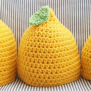Puede incluir: Tres gorros de punto de lim&oacute;n en diferentes tama&ntilde;os, todos amarillos con hojas verdes en la parte superior.