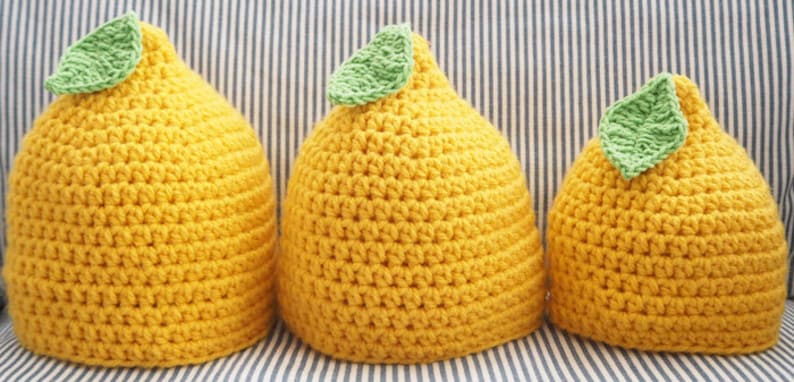 Puede incluir: Tres gorros de punto de lim&oacute;n en diferentes tama&ntilde;os, todos amarillos con hojas verdes en la parte superior.