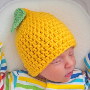 Puede incluir: Un gorro de punto amarillo en forma de lim&oacute;n con una hoja verde en la parte superior. El gorro lo lleva puesto un beb&eacute; dormido.