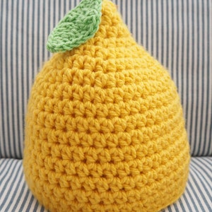 Puede incluir: Un gorro de punto de lim&oacute;n con una hoja verde en la parte superior. El gorro es amarillo y tiene una superficie texturizada.