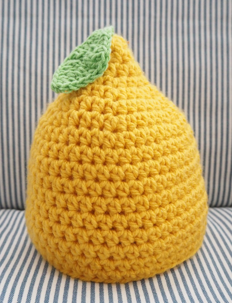 Puede incluir: Un gorro de punto de lim&oacute;n con una hoja verde en la parte superior. El gorro es amarillo y tiene una superficie texturizada.