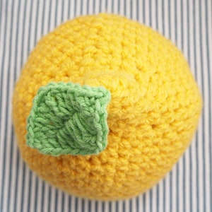 Puede incluir: Un gorro de punto de lim&oacute;n con un detalle de hoja verde. El gorro es amarillo y tiene una superficie texturizada.