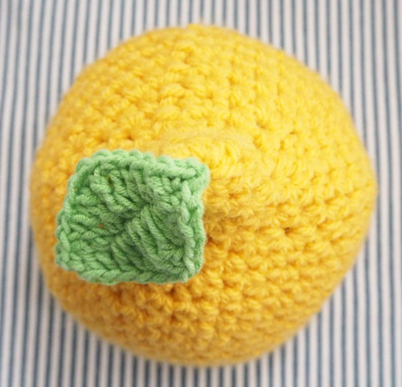 Puede incluir: Un gorro de punto de lim&oacute;n con un detalle de hoja verde. El gorro es amarillo y tiene una superficie texturizada.
