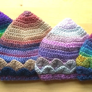 K&ouml;nnte beinhalten: Vier bunte H&auml;kelm&uuml;tzen mit einem gewellten Rand. Die M&uuml;tzen sind in den Farben Lila, Gr&uuml;n, Rosa und Blau.