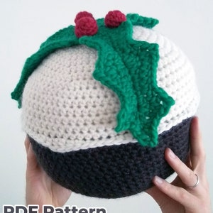 May include: A crocheted Christmas pudding ornament with a green holly leaf and red berries on top. The pudding is white with a black bottom.