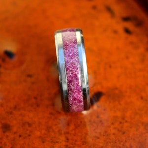 Puede incluir: Un anillo de plata con una incrustación rosa y blanca. El anillo está hecho de metal y tiene un acabado pulido.