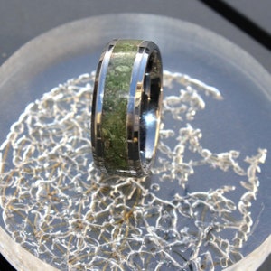 Puede incluir: Un anillo de plata con una incrustación verde. El anillo está sobre una superficie blanca.