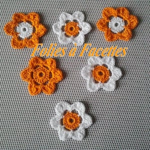 Peut inclure: Six fleurs crochetées en orange et blanc. Les fleurs ont cinq pétales et un petit centre orange. Les fleurs sont disposées en forme de cœur sur un fond blanc.
