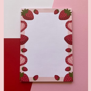 May include: A white notepad with a pink border and a strawberry design. The strawberries are red with green leaves and are arranged around the border of the notepad.
