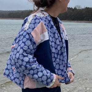 May include: A blue and pink patchwork jacket with a white floral pattern on the shoulder. The jacket has a blue and white polka dot pattern on the front and sleeves.
