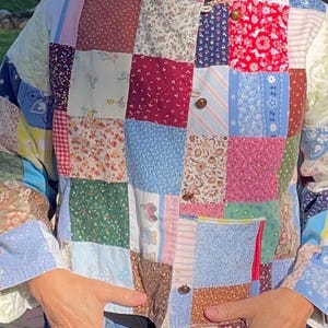 May include: A patchwork jacket with a variety of fabric patterns and colors, including floral, paisley, and solid squares. The jacket has a round collar, long sleeves, and button closures. The jacket is made of quilted fabric.