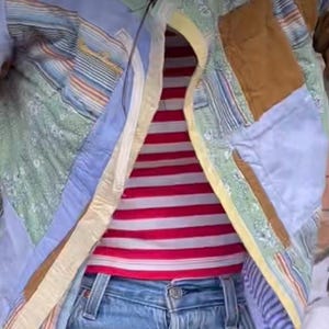 Puede incluir: Una chaqueta de patchwork azul y amarilla con cierre de cremallera. La chaqueta se lleva sobre una camisa a rayas rojas y blancas y unos vaqueros azules.